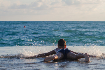 The boy lies on the edge of the pier near the sea. A boy is playing with big waves and big splashes on the pier. Sunset, closeup, selective focus