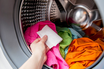 Woman hand put color absorbing sheet inside a washing machine, allows to wash mixed color clothes...