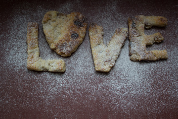 The cookies made with own hands on a red background, sprinkled with flour. Letters from the LOVE test. It can be used in a web design, the menu, the calendar.