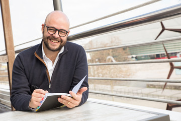 Smiling middle-aged man making notes in street cafe