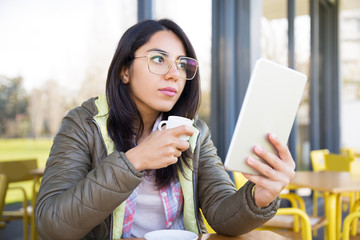 Serious lady using tablet and drinking coffee in cafe