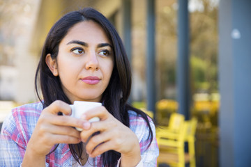 Serious pretty young woman enjoying drinking coffee in cafe