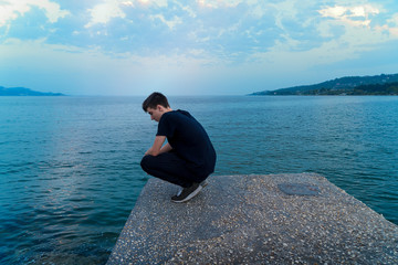 young man crouching on a pier, looking into the sea