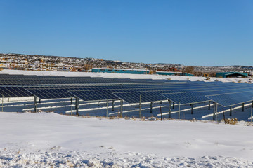 Obraz premium Solar panels on solar power station in snow covered mountains and white clouds in the background.