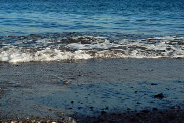 Rocky coast of the sea. Waves on the beach. Blue sea water.