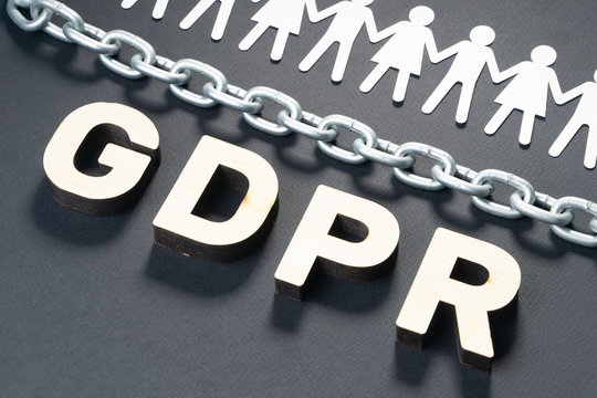 Wooden GDPR letters in front of human paper figures and metal chain. General data protection concept.