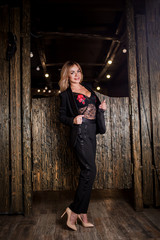 Full length portrait of glamorous sensual beautiful blonde woman posing in black pant suit and lace lingerie in front of wooden wall. Underwear, clothes, fashion, sexy