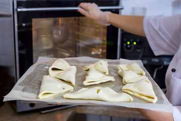 Woman cook lays cheese puffs on baking sheet in oven. Fresh pastries in the cafe