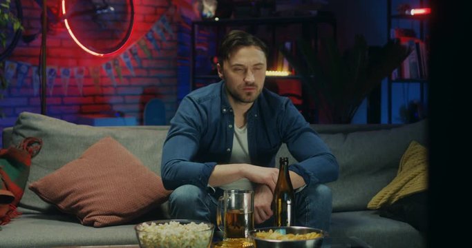 Handsome of the Caucasian young man watching TV at night and drinking beer, sport fan watching a game.