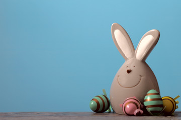 On a wooden beige surface, an Easter bunny and a group of colorful bright eggs on a blue background. Cut off picture, horizontal, free space for text, side view. Easter concept.