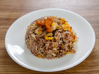 Fried brown rice with eggs and sausages on white dish.