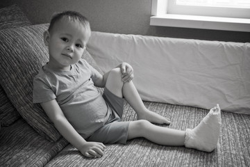 Broken leg in cast of little boy. Little Child Boy With Plaster Bandage On Leg foot fracture. Human Healthcare And Medicine Concept. Black-and-white photo