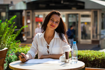 Elegant girl calling someone while resting in outdoor cafe with cup of coffee