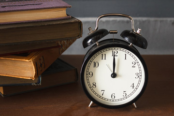 piles of different old books on a dusty table and an alarm clock