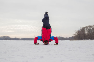Fototapeta na wymiar A middle-aged man is engaged in yoga on a frozen river. Shirshasana(Headstand)