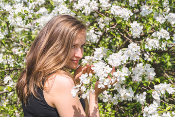 Naklejka premium Beautiful woman among flowers of spring blossoming trees in the garden