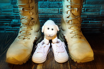 Military army boots and baby shoes.Family and country protection concept.Stone wall in the background