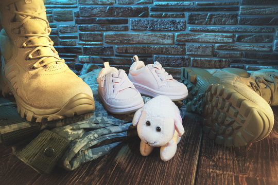 Military Army Boots And Baby Shoes.Family And Country Protection Concept.Stone Wall In The Background