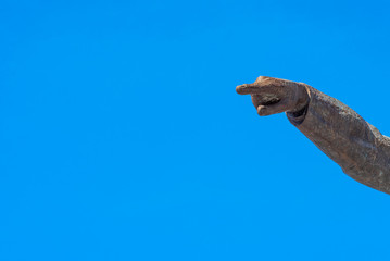 Stone hand with pointing finger and blue sky in the background