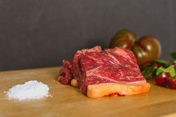 Slices of fresh raw beef steak on wooden board on black background with salad and tomatoes