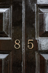 House number eighty five with the 85 in bronze lettering on a black wooden painted and carved house door in the cross section