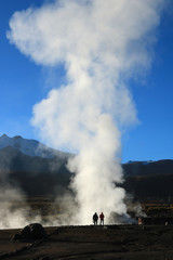 Two people walking to smoke column in El Tatio Geysers