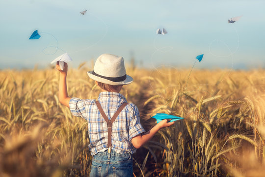 Cute Boy In A Hat Throwing A Paper Airplane. Child In A Wheat Field.