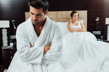 Fototapeta premium selective focus of handsome man sitting with crossed arms near girlfriend after quarrel
