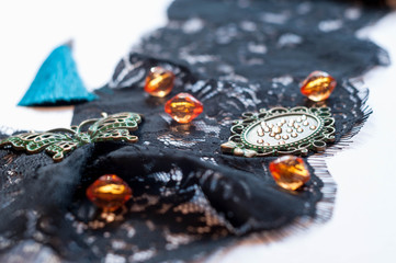 selective focus of black ornament lace with glass orange beads, green small frame, rhinestones, decorative butterfly and blue tassel on white