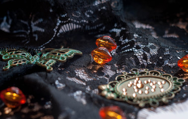 selective focus of glass beads, green small frame with rhinestones and decorative butterfly on black lace on white