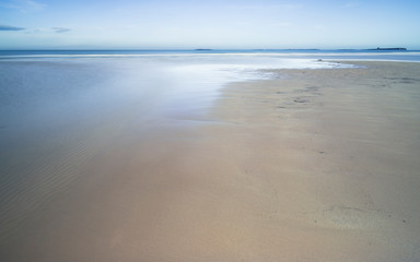 A tranquil scene of the beach at Bamburgh, Northumberland, with sand and a stream flowing towards the sea.