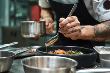 Foto op Plexiglas Geheim recept. Close-up foto van chef-kok handen met verschillende tatoeages die een saus toevoegen aan Italiaanse pasta Carbonara. © Friends Stock