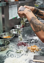 Traditional recipe. Cropped vertical image of chef's hands with beautiful tattoos making traditional italian pasta in restaurant kitchen