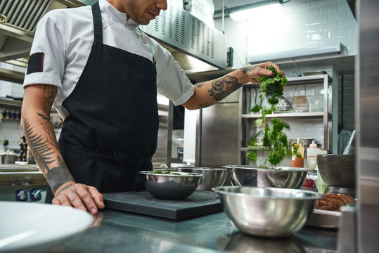 Vegetarian food. Close-up of chef hands with beautiful tattoos preparing salad in a restaurant kitchen