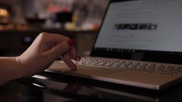 woman hand with manicure scrolls news feed on a laptop, close up