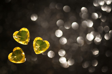 Shiny yellow, heart shape glass, jewelry, placers on a black background with blurred spots.