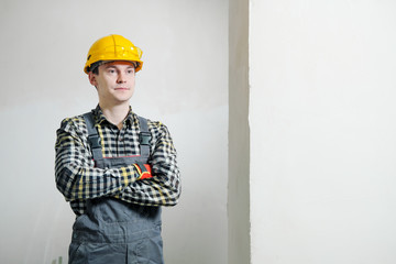 Portrait of a young male builder and repairman in a yellow helmet against the background of a wall.