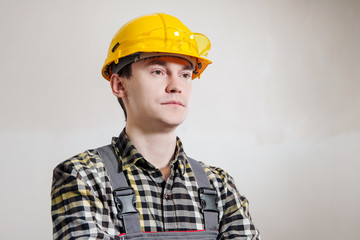 Portrait of a young male builder and repairman in a yellow helmet against the background of a wall.