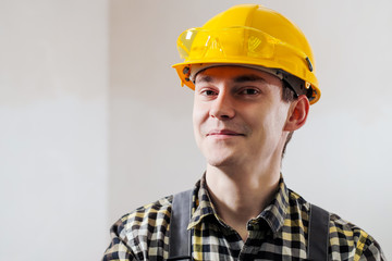 Portrait of a young male builder and repairman in a yellow helmet against the background of a wall.