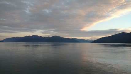 Sunset over the Pacific Ocean setting below a mountain range with bright colors gleaming off the clouds and ocean