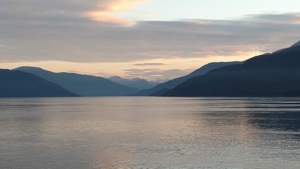 Sunset over the Pacific Ocean setting below a mountain range with bright colors gleaming off the clouds and ocean