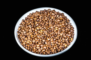 Coffee beans on a round plate close up. Isolated on black background.