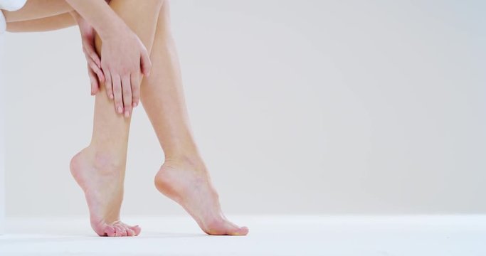 Slow motion close up of young woman touching her perfect  hairless soft and silky legs after depilation isolated on a white background. 