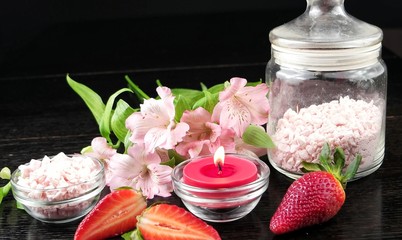 Strawberries, aromatic salt, pink flowers and a candle on a black background. Spa and aromatherapy