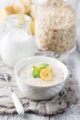 Bowl of oatmeal porridge with banana on white wooden rustic table, healthy breakfast, diet food.