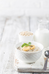 Bowl of oatmeal porridge with banana on white wooden rustic table, healthy breakfast, diet food.