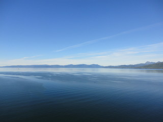Calm Pacific Ocean in the inside passage in Alaska blue sky meets mountains and blue sea in a peacefully clear view
