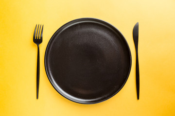 Black ceramic plate with knife and fork on yellow background. Pop art design