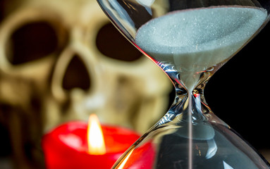 an hourglass, a candle and a skull are on a table. Concept tearing time.