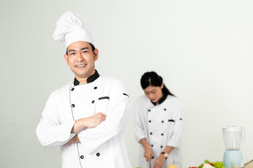 Confident Asian chef looking at camera with his helper background
